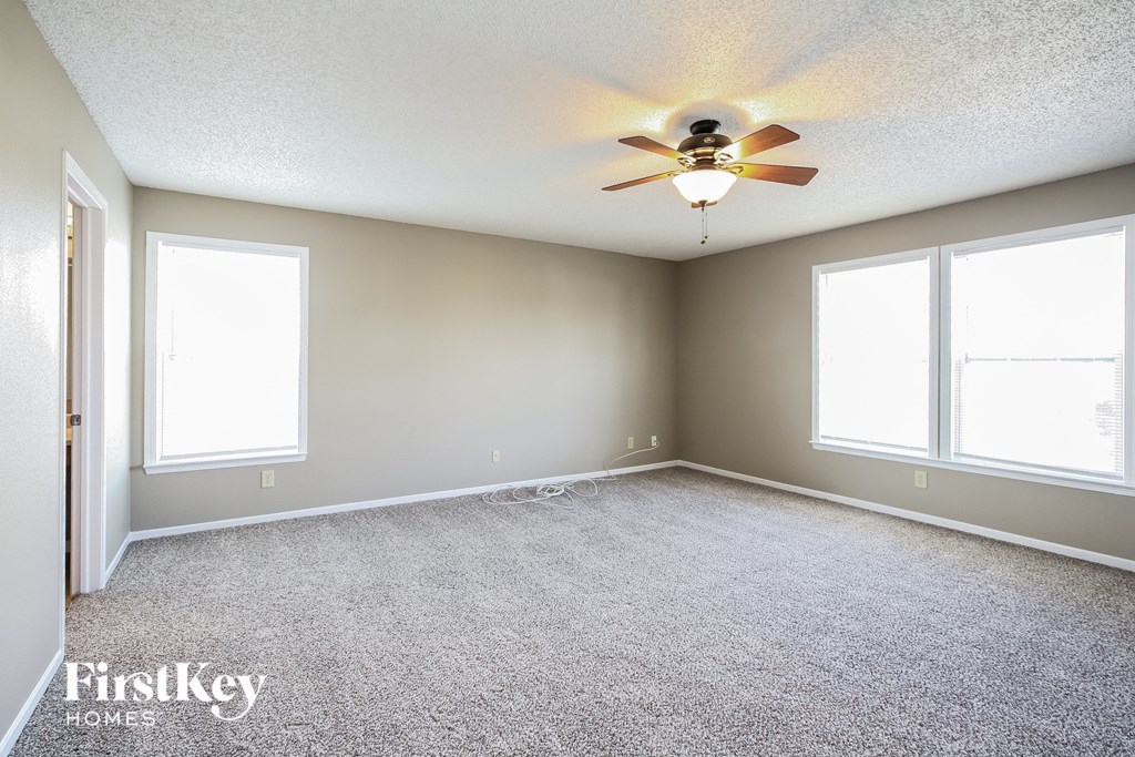 an empty living room with a ceiling fan and three windows