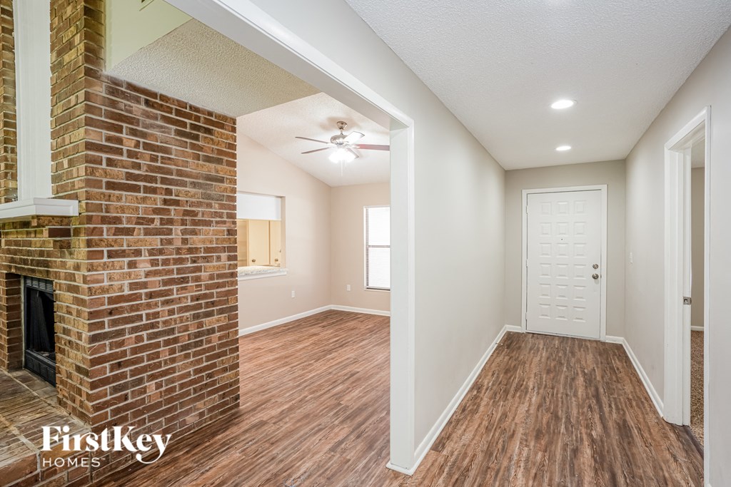 an empty living room with a brick fireplace and a door to the bathroom