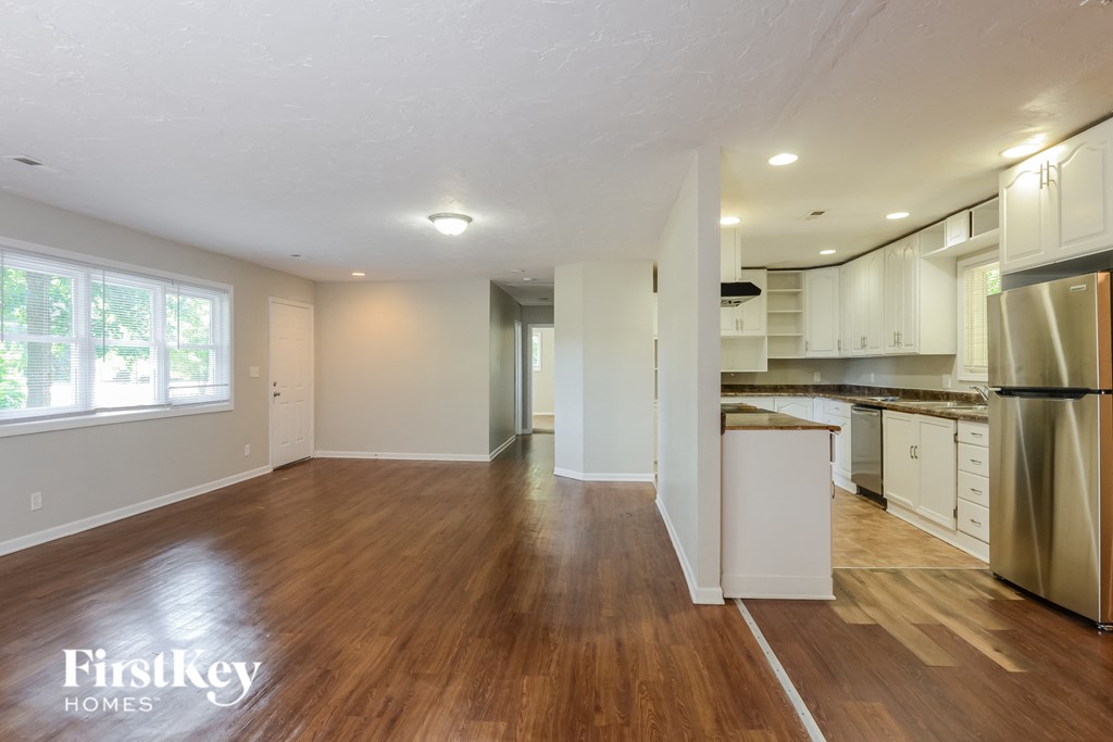 an empty kitchen and living room with hardwood flooring and a stainless steel refrigerator