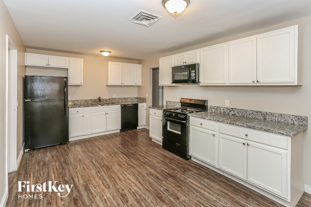 A kitchen with a black fridge, black oven, and white cabinets.