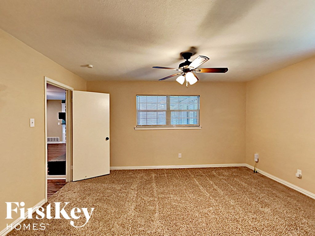 an empty living room with a ceiling fan and a door to a bathroom
