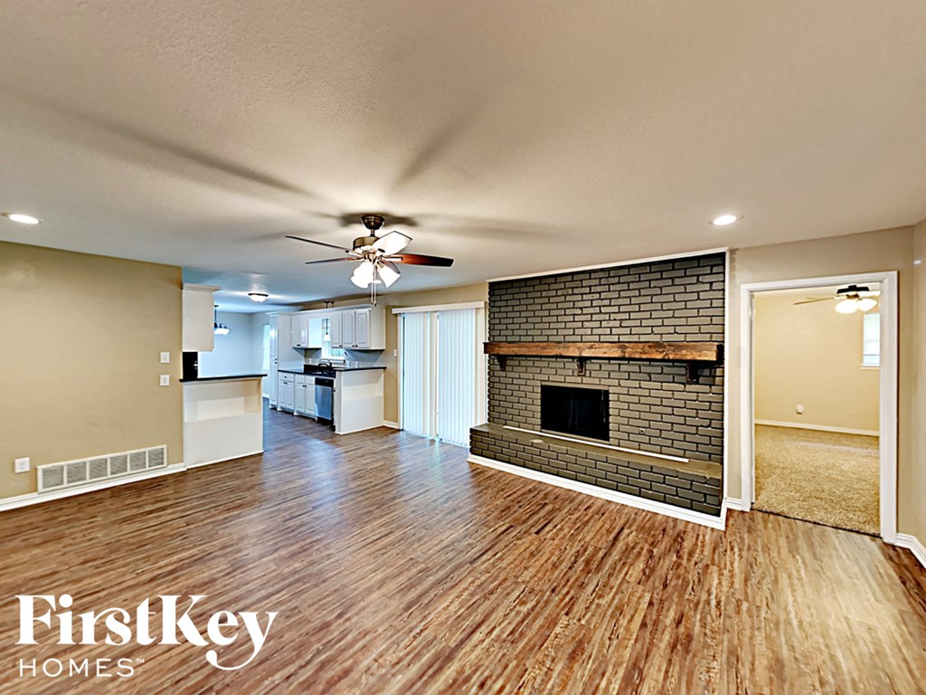 an empty living room with a brick fireplace and a ceiling fan