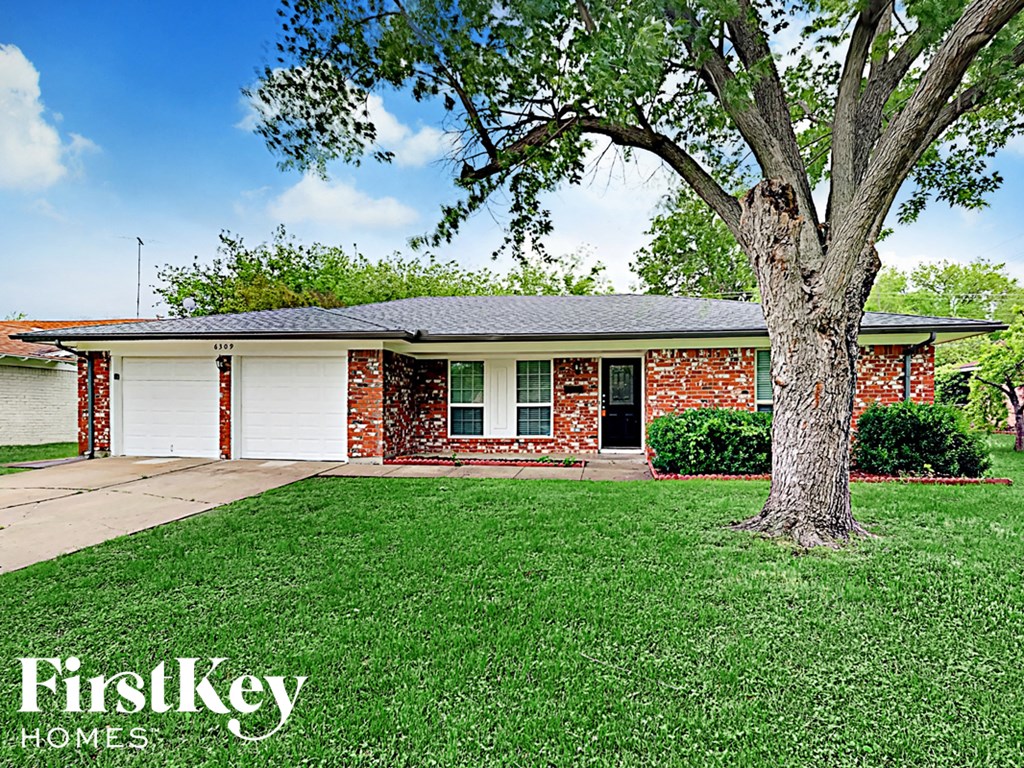 the front of a brick house with a tree in the yard