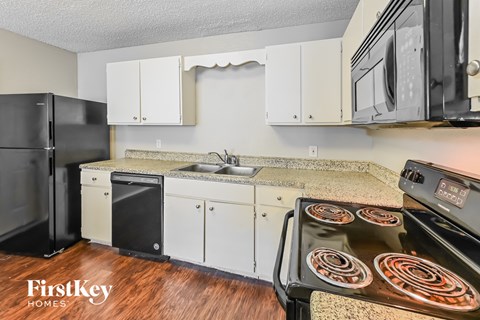 A kitchen with a black fridge, white cabinets, and a stove top oven.