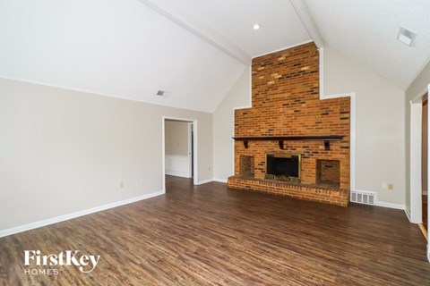 A large empty room with a brick fireplace and wooden floors.