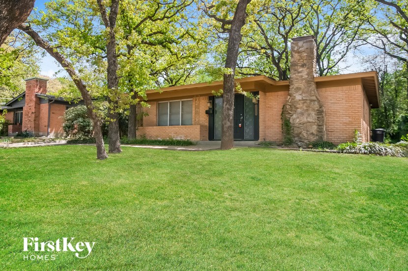 a brown brick house with a green lawn and trees