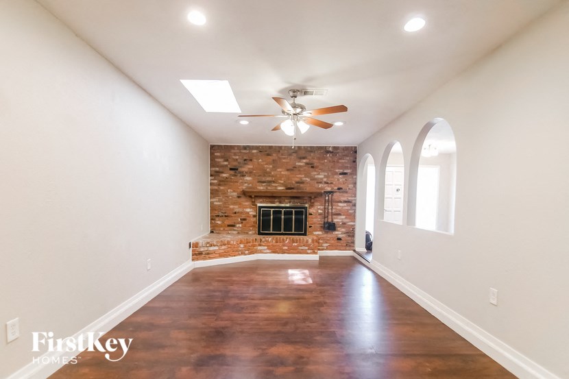 an empty living room with a brick fireplace and a ceiling fan