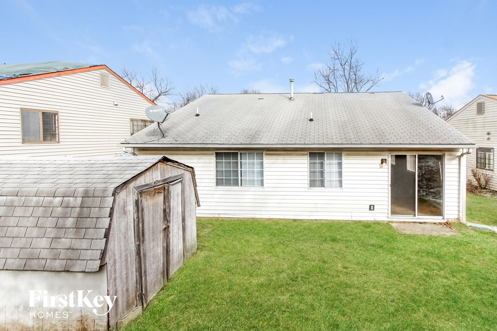 the back of a white house with a shed and a roof on the grass