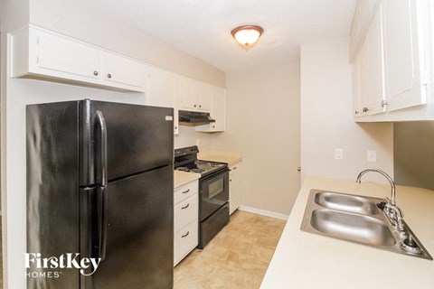 A kitchen with a black refrigerator and a sink with two faucets.