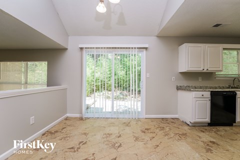 A kitchen area with a black dishwasher and a window with blinds.