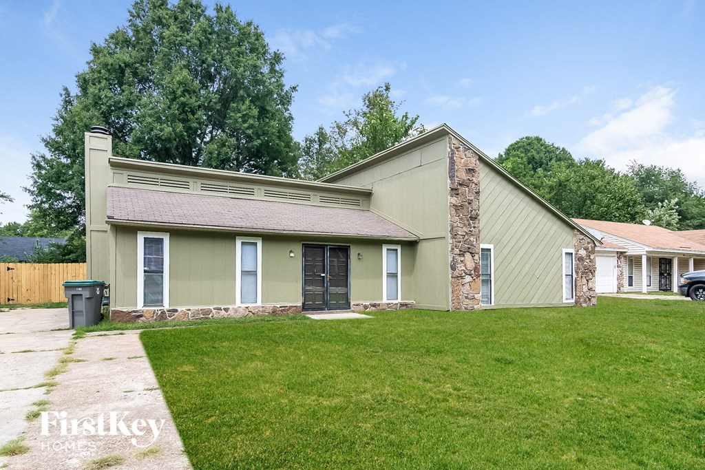 a green house with a grassy yard and a driveway