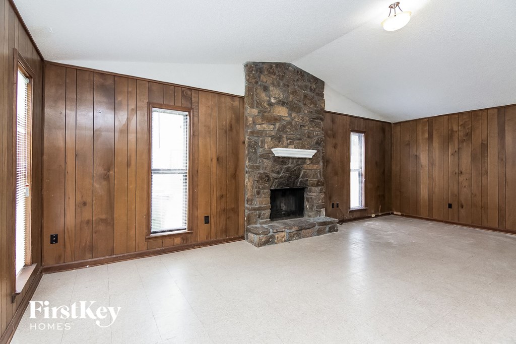 an empty living room with a stone fireplace and wooden walls