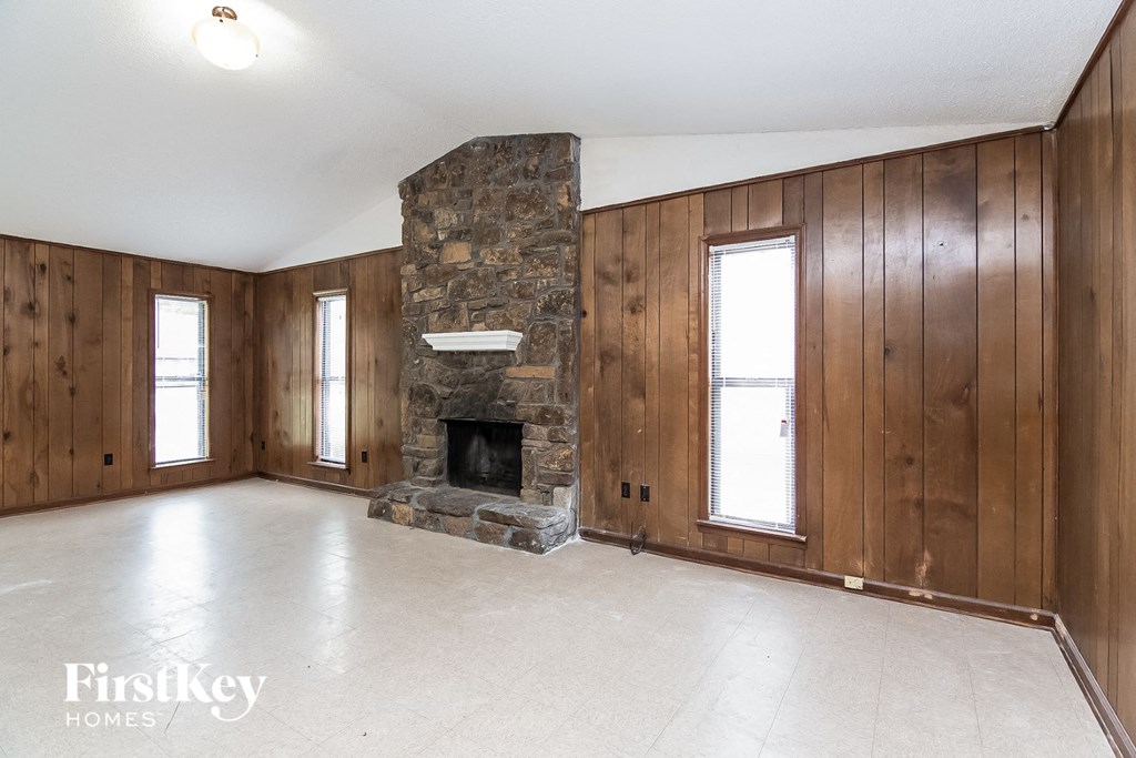 an empty living room with a stone fireplace and wooden walls