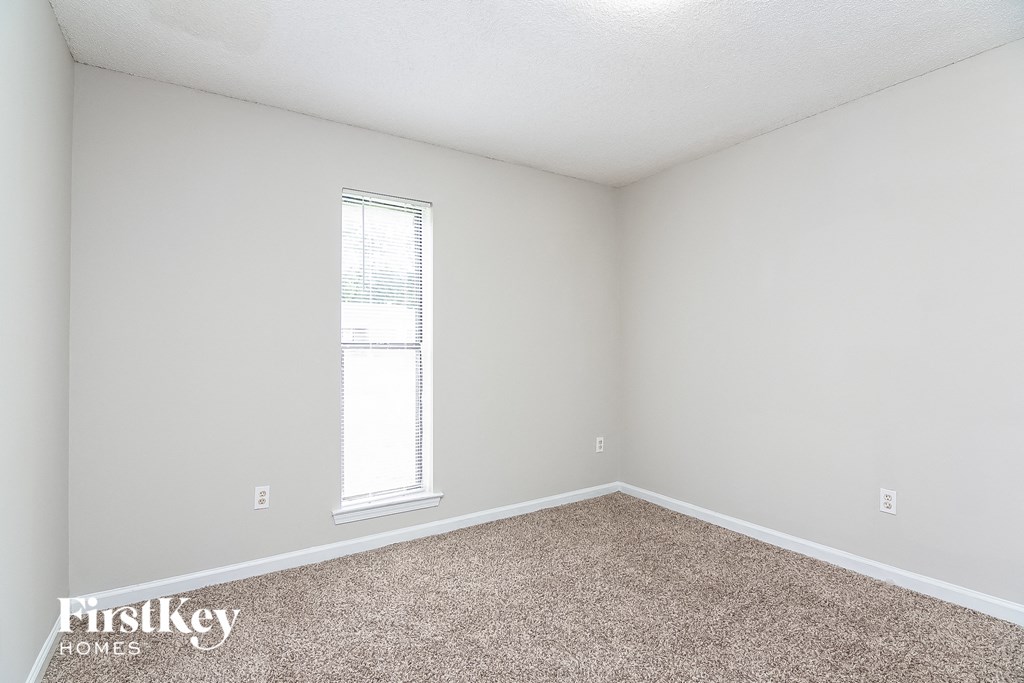 a bedroom with white walls and carpet and a window