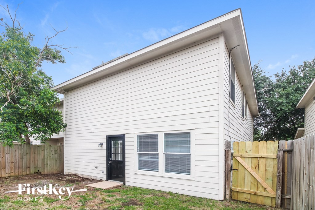 the backyard of a small white house with a wooden fence