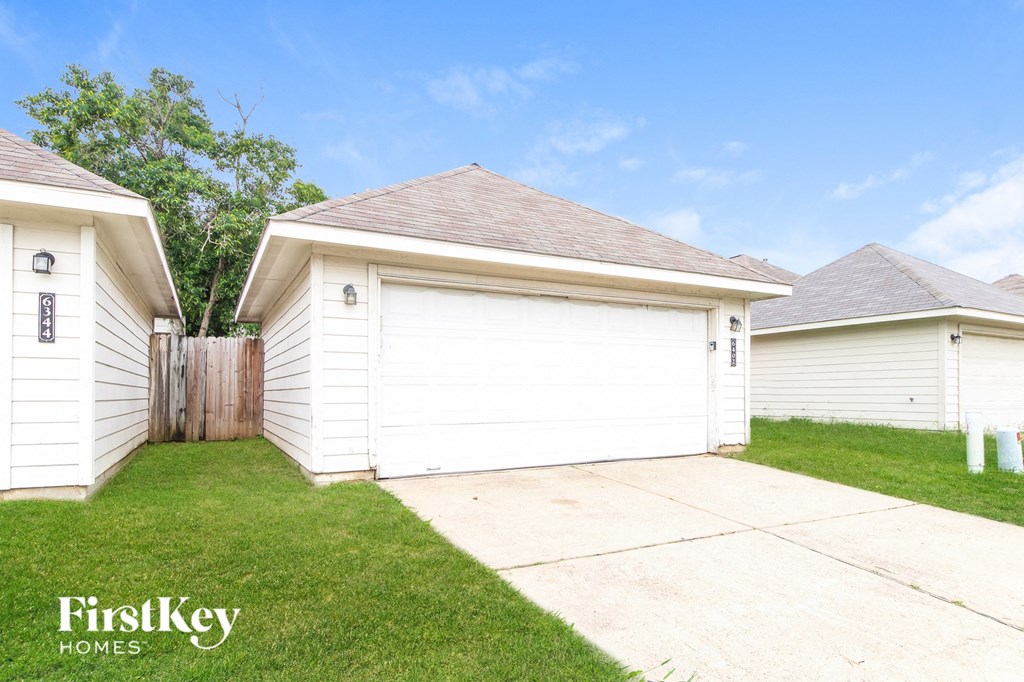 the backyard of a white garage with a driveway and a fence