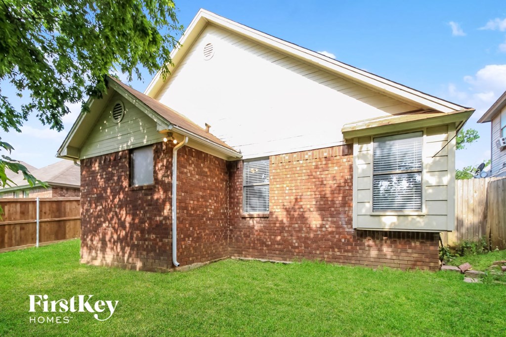 the front of a brick house with green grass and a wooden fence