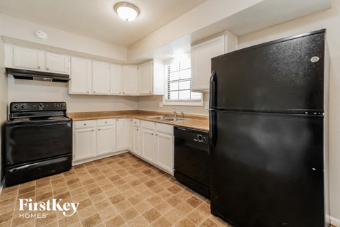 A black refrigerator in a kitchen with white cabinets.