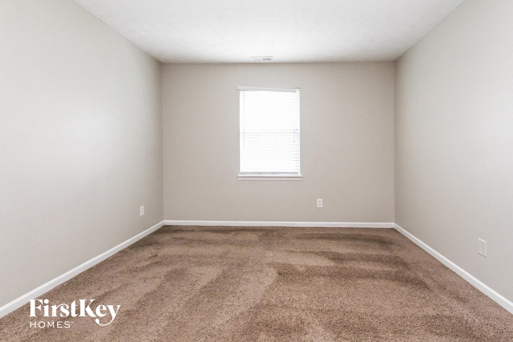 a carpeted room with a window and white walls