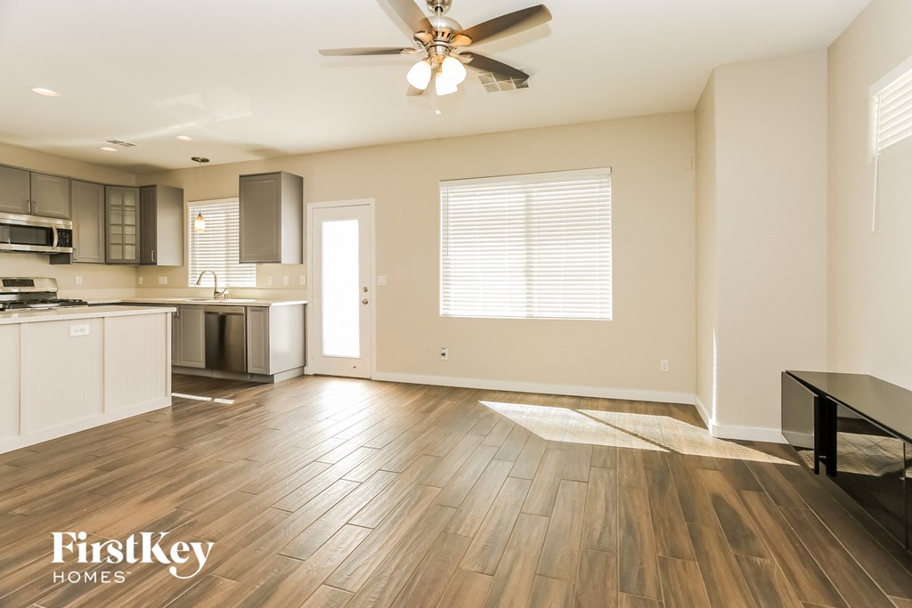 an empty living room and kitchen with wood flooring and a ceiling fan