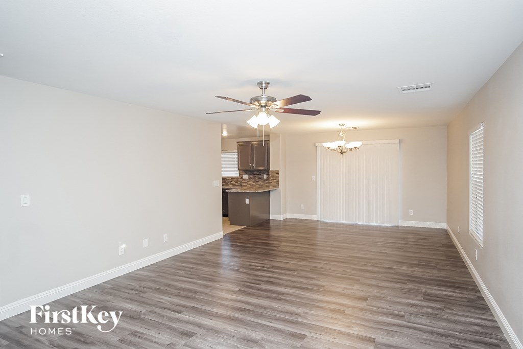 an empty living room with a ceiling fan and a kitchen