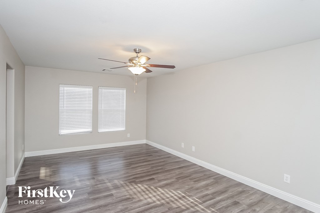 the spacious living room with wood flooring and a ceiling fan
