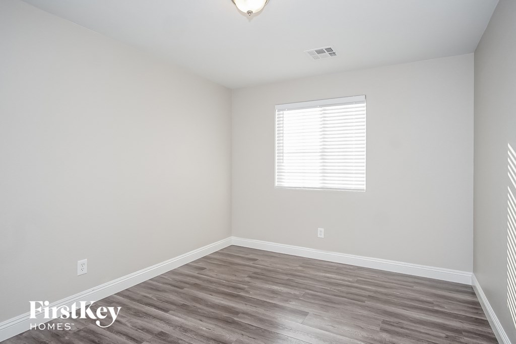 a bedroom with white walls and wood floors and a window
