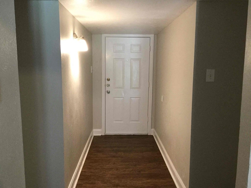 A white door is at the end of a hallway with lights on the wall.