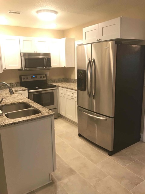 A black refrigerator stands next to a sink in a kitchen.