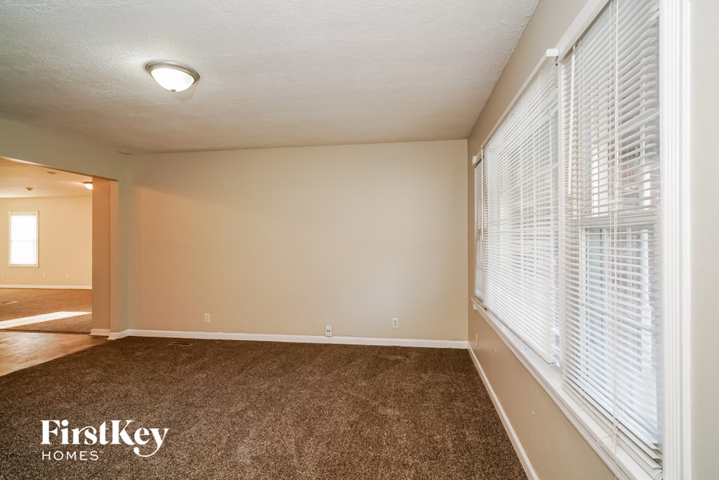 the spacious living room with large windows and carpeted flooring