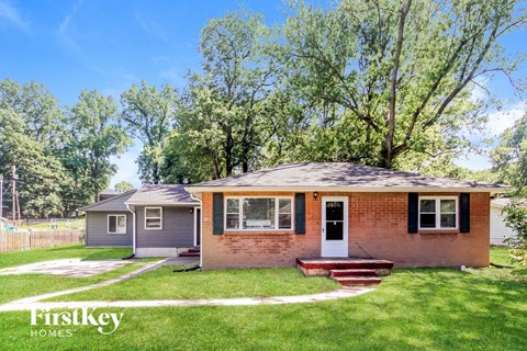 a small brick house with a front lawn and trees