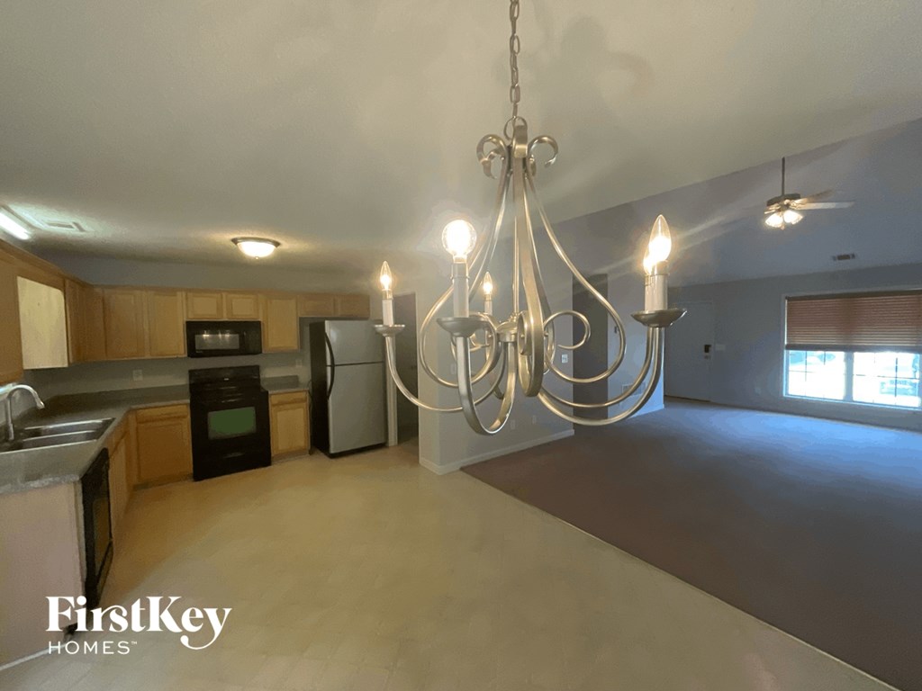 A chandelier hangs over a kitchen island with a sink and a refrigerator.