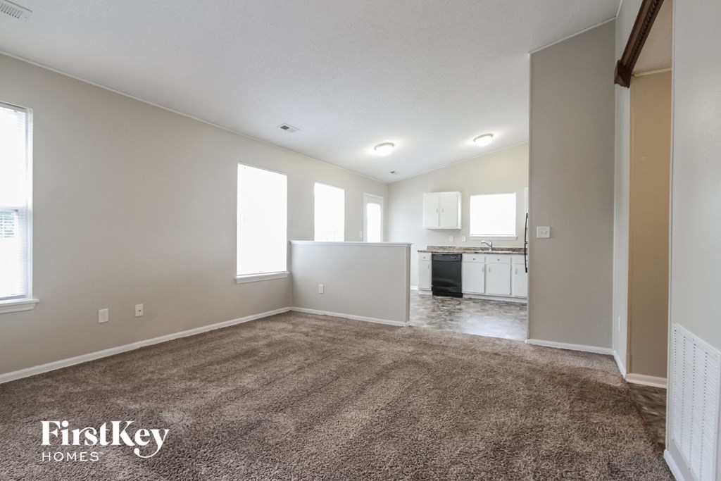 an empty living room with carpet and a kitchen