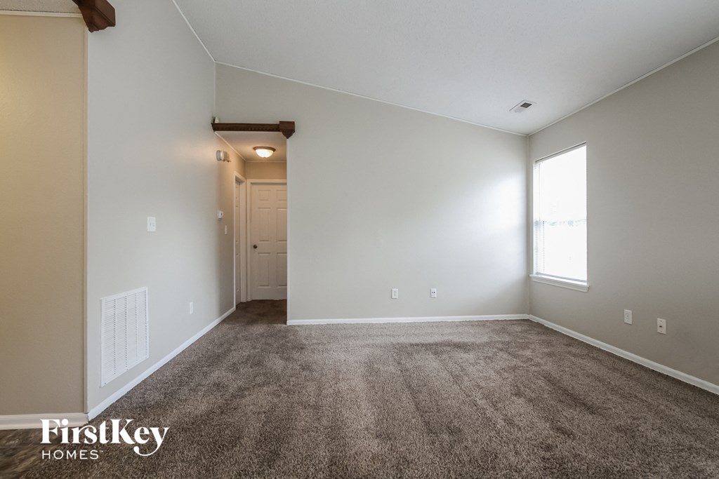 a living room with carpet and white walls and a window