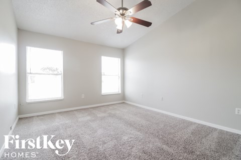 A spacious room with a ceiling fan and two windows.