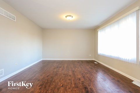 A room with wooden flooring and a window with white curtains.