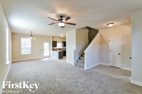 an empty living room with a ceiling fan and a kitchen