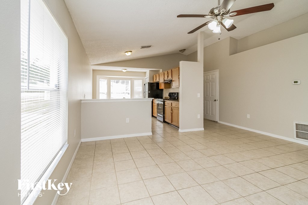 A spacious living room with a fan and a kitchen in the background.