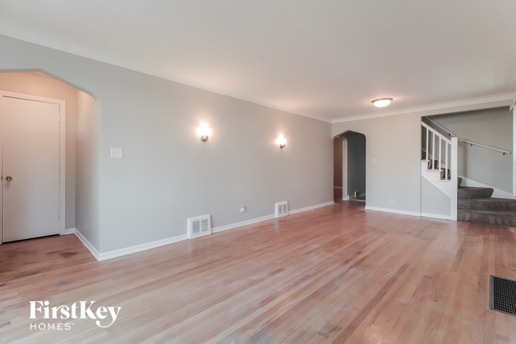 A room with wooden floors and a staircase in the background.