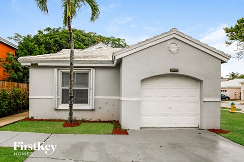 A small house with a garage door and a palm tree in front.