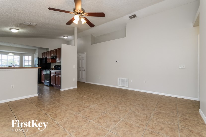 A spacious room with a ceiling fan and light fixture, and a kitchen area visible through the doorway.