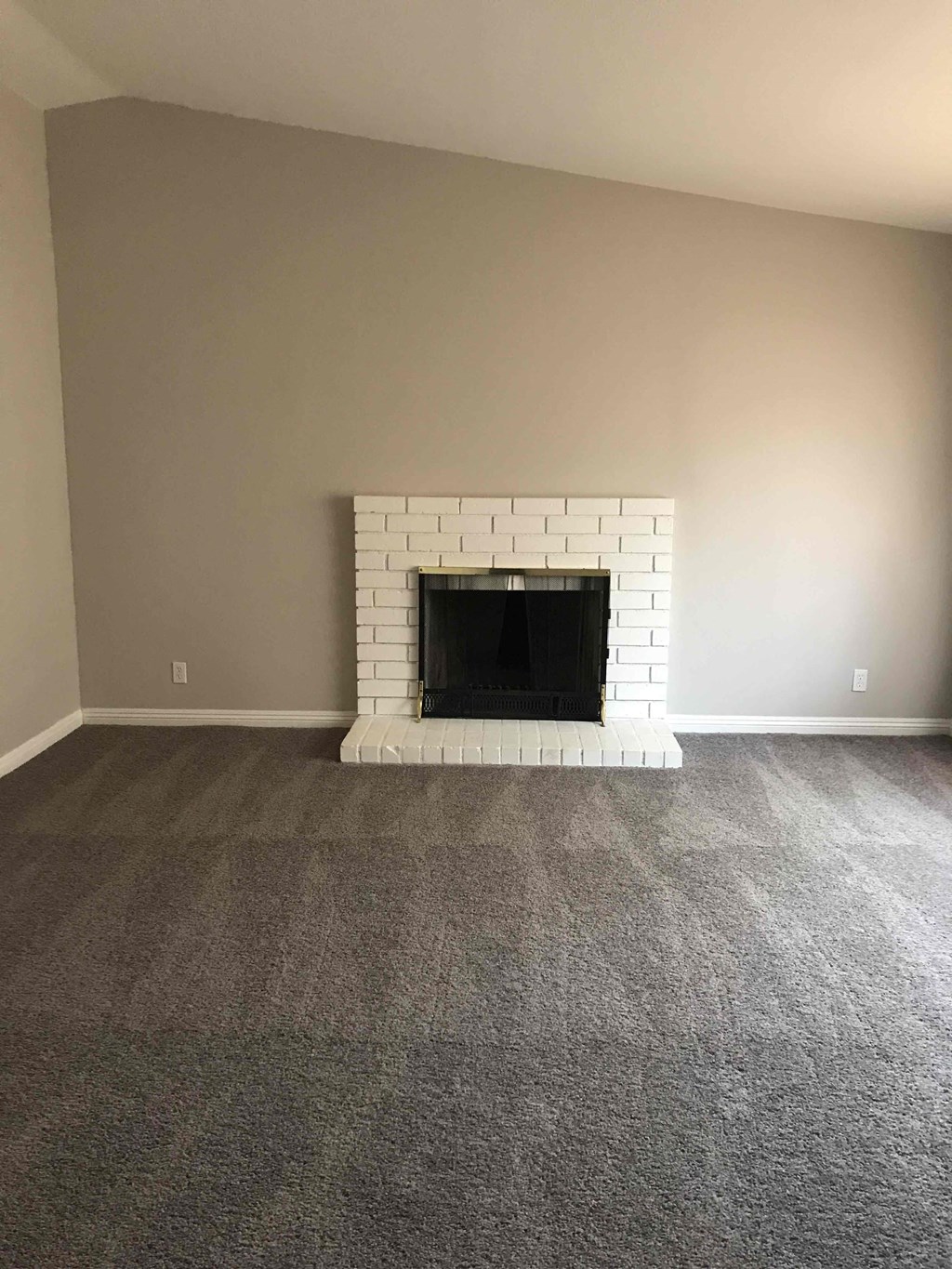 A white brick fireplace in a room with grey carpet.
