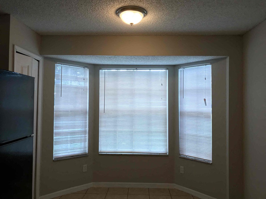 A kitchen with a refrigerator and a window with blinds.
