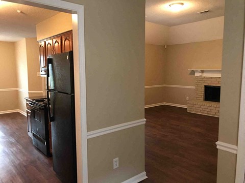A black refrigerator is in a kitchen with wood floors and a brick fireplace.