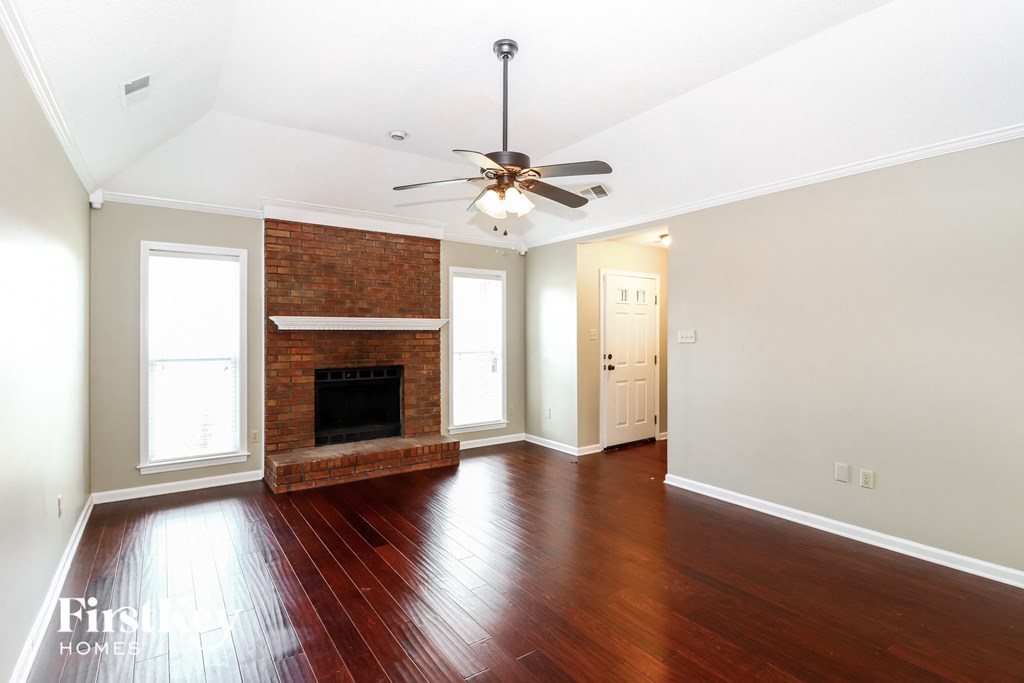 an empty living room with a brick fireplace and a ceiling fan