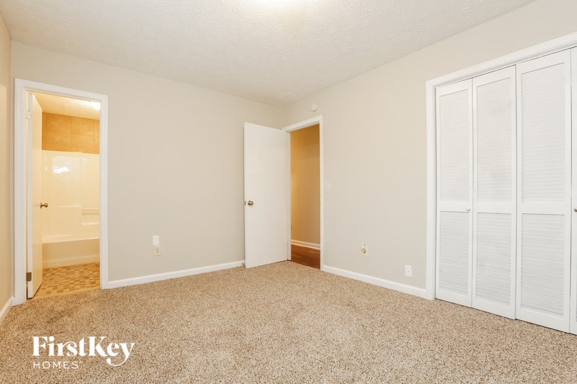A sparsely furnished bedroom with a white door and a white closet.