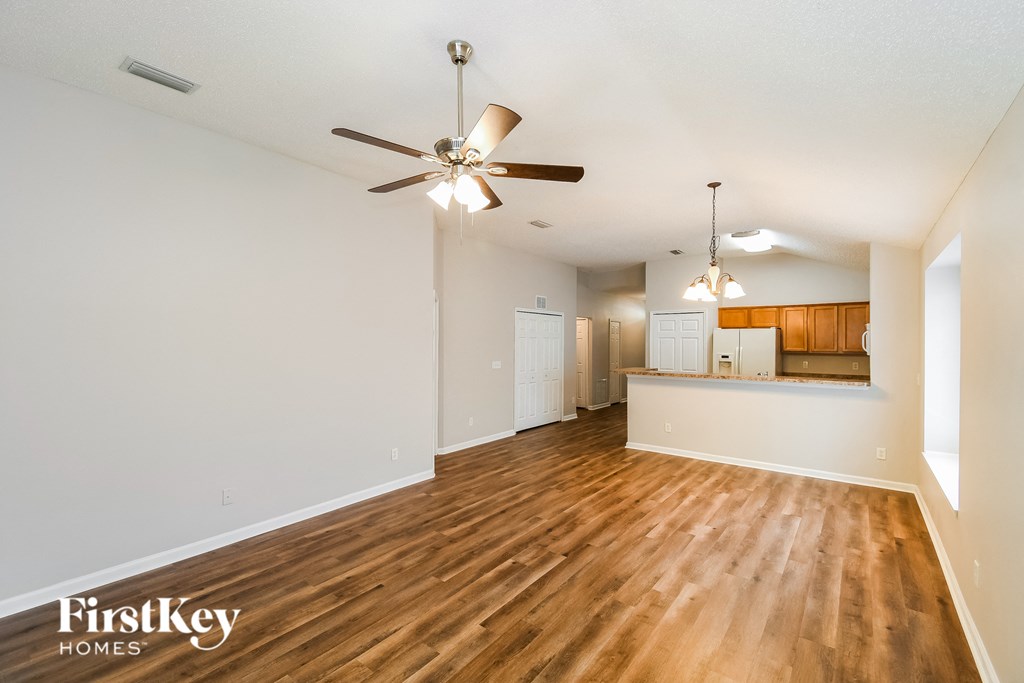 an empty living room with a ceiling fan and a kitchen