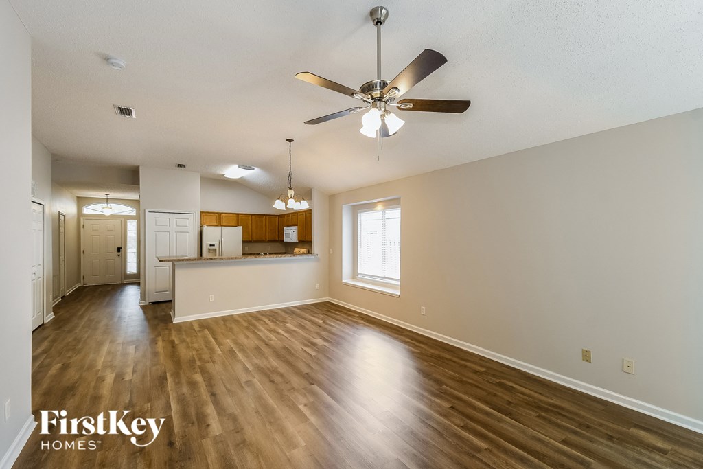 an empty living room with a ceiling fan and a kitchen
