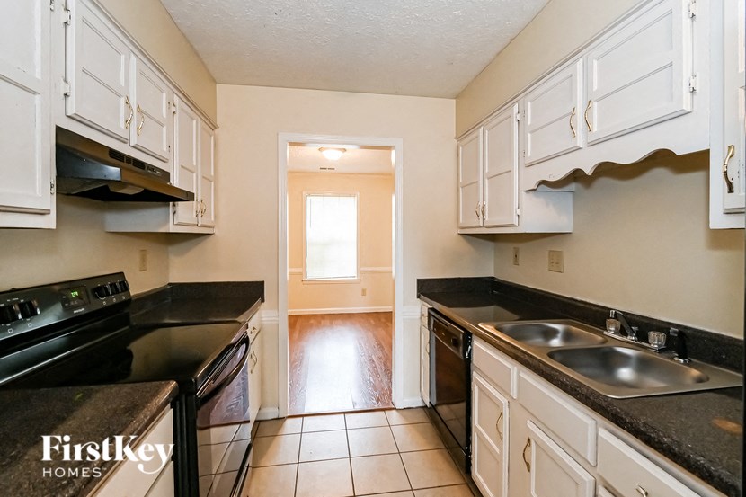 a kitchen with black counters and white cabinets and a door to a hallway