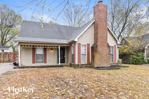 the front of a house with a brick chimney and a yard with fallen leaves